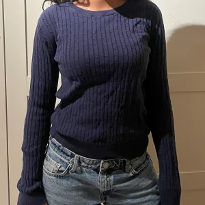 Mörkblå ribbstickad tröja - Mörkblå ribbstickad tröja med rund halsringning och långa ärmar. Tröjan har en klassisk, smal passform och är perfekt att matcha med jeans. Materialet känns mjukt och följsamt, vilket gör den både snygg och bekväm.