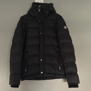 Svart Moncler jacka  - Svart dunjacka från Moncler med klassisk puffer-design, huva och dragkedja framtill. Jackan har två fickor med dragkedja och ikoniskt Moncler-märke på ärmen. Perfekt nu till vintern. Storleken är S men passar även M. Pris kan diskuteras..!
