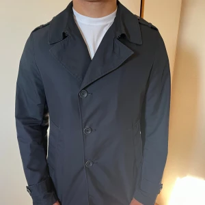 Herno overshirt/rock - Snygg mörkblå rock/ocershirt med klassisk krage och knäppning framtill. Jackan har raka linjer, axelklaffar och diskreta sidfickor. Perfekt för dig som gillar stilren och tidlös design. Passar till både skjorta och t-shirt. Den har en defekt med en söndrig knapp på ena ärmen. 