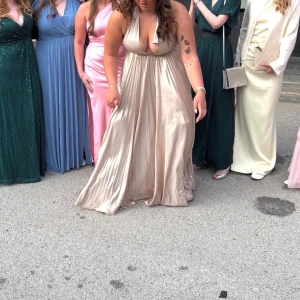 Champagnefärgad långklänning Bubbleroom - Superfin långklänning från Bubbleroom i skimrande champagnefärg. Djup v-ringning, plisserad kjol och bred midja som markerar siluetten. Klänningen är ärmlös och har en elegant, flowy look som verkligen sticker ut. Endast använd under studentbalen! Ny pris 1599