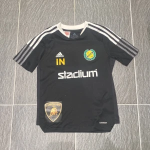 Svart IK Sävehof handbolls t-shirt Adidas - Svart handbolls t-shirt från Adidas med IK Sävehof-logga på bröstet, vita ränder på axlarna och vit krage. Tryck med Stadium, Lamborghini och gula detaljer. Tillverkad i Primegreen-material som andas.