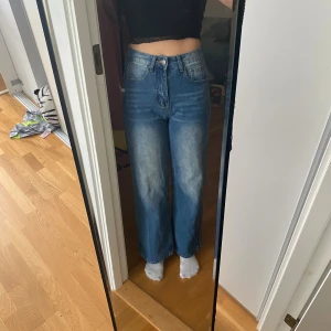 Blåa wide high waist jeans - Säljer ett par blåa jeans med hög midja och breda ben. Jeansen har klassisk femficksdesign, ljusare tvätt framtill och baktill samt raka, vida ben. Perfekta för en chill och trendig look.