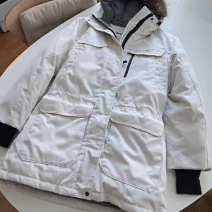 Vit dunparkas från Everest, strl 40 - Säljer en vit parkajacka från Everest i storlek 40. Jackan har huva med fuskpäls, stora fickor framtill och dragkedja. Yttertyg i polyester, fodrad med nylon och fylld med 70% dun och 30% fjäder. Perfekt för kalla dagar och riktigt snygg passform.