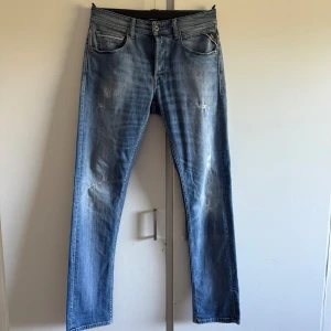 Replay ljusblå jeans straight fit - Snygga Replay Grover jeans i ljusblå tvätt med slitningar och raka ben. Klassisk femficksmodell med Replay-logga på myntfickan och bakficka. Jeansen är gjorda i bomull och har en avslappnad, rak passform som funkar till allt. De är knappt använda. 