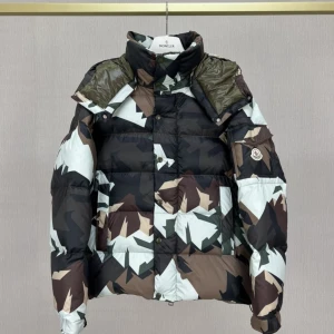 Moncler camo dunjacka med dragkedja - Snygg dunjacka från Moncler med coolt camouflage-mönster i svart, brunt, beige och grönt. Jackan har hög krage, dragkedja och tryckknappar, samt Moncler-logga på ärmen. Insidan är olivgrön och jackan är vadderad för extra värme.