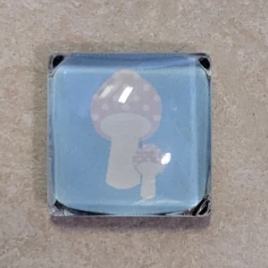 Magnet med svampmotiv - Söt fyrkantig magnet med ljusblå bakgrund och två vita svampar med prickar. Perfekt att använda som kylskåpsmagnet eller som dekoration 