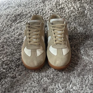 Maison Margiela Sneakers - Maison Margiela sneakers i beige mocka och vitt skinn med klassisk gummisula. Snygg retrostil med snörning och rund tå. Perfekta för dig som gillar minimalistisk och stilren design med lyxig känsla. Tveka inte att höra av dig vid frågor eller fler bilder!
