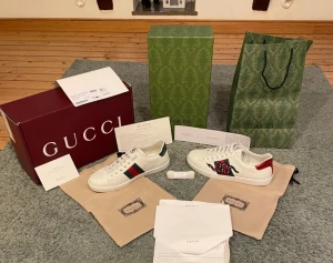 Gcci Ace sneakers med orm och ränder - Säljer ett par Gcci Ace sneakers i vitt skinn med klassiska gröna och röda ränder på sidorna. Ena skon har en broderad röd och svart orm, medan den andra har en röd hälflik i metallic. Platt sula och rund tå, med snörning. Obs inget og ingår