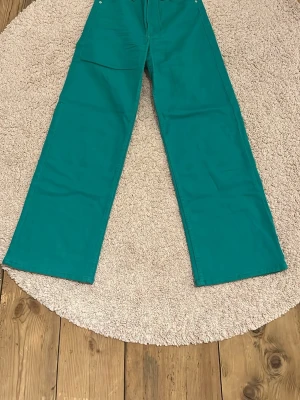 Turkosa wide byxor från H&M Divided - Snygga turkosa byxor från H&M Divided i storlek 38. Modellen är wide med raka, breda ben och klassisk femficksdesign. Tillverkade i mjuk bomull som känns skön mot huden. Perfekt för dig som vill sticka ut med färg och stil.