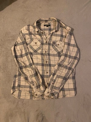 Beige rutig skjorta från Mywearman - Säljer en beige skjorta från Mywearman i storlek S med svart och grått rutmönster. Skjortan har två bröstfickor med knappar, klassisk krage och långa ärmar. Materialet är mjuk bomull som känns skönt mot huden. Perfekt för dig som gillar avslappnad stil.