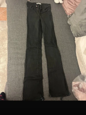 Svarta jeans med slits  - Svarta jeans med bootcut-snitt och slitsar längst ner på benen. . Klassisk femficksmodell och tillverkade i jeansmaterial. Perfekta för dig som gillar att sticka ut med detaljer. Väldigt slitna i änden därav låga priset.