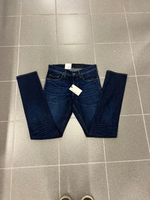 Mörkblå  jeans från Tiger of sweden W28 L32 - Snygga mörkblå jeans från Tiger of sweden med klassisk femficksdesign och raka ben. Jeansen har kontrastsömmar, läderpatch med logga bak och en smal fot. Perfekt passform för dig som gillar stilrena och tidlösa jeans.