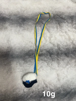 Studentmössa med blågul band - Säljer en liten virkad studentmössa med blått och gult band att hänga runt halsen. Mössan är vit och svart med en liten blå detalj framtill. Perfekt som accessoar till studentfirandet eller som dekoration.🌸 Att hänga runt halsen vid student. Köpt av en som tillverkar själv 