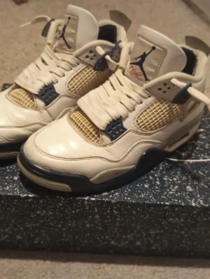 Nike Air Jordan 4 Retro Vit/Blå - Nike Air Jordan 4 Retro sneakers i vit och marinblå med inslag av beige och röda detaljer på sulan. Skorna har snörning, meshpaneler och speckled midsole. Ikonisk Jumpman-logga på plösen och hälen. Tillverkade i skinn och syntetmaterial, med platt sula och rund tå. Jag har även lappat hälen så att hålet i hälen inte syns. Detta är en Intressekoll så skriv till mig vid intresse 