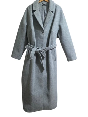 Grå kappa med bälte från Xlnt - Snygg grå kappa från Xlnt i storlek 2XL. Klassisk modell med krage, två knappar framtill och ett matchande bälte i midjan. Långärmad och med slät yta, perfekt för dig som gillar stilrena och tidlösa plagg. Fodrad insida för extra komfort. Helt ny och oanvänd, köpt för 1500kr