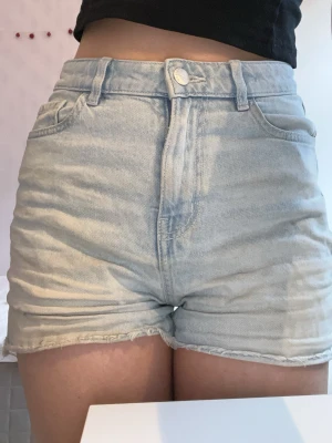 Ljusblå denim/jeanshorts från lindex - Säljer ett par ljusblå denimshorts från lindex med hög midja och fransiga kanter. Shortsen har knapp och dragkedja framtill. Perfekta för varma dagar och har en loose passform som är chill och bekväm. Shortsen är ganska korta 