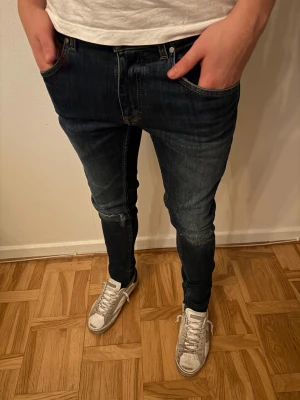 Tiger of sweden Jeans - Snygga mörkblå jeans från T/J med skinny/slim passform och klassisk femficksdesign. Jeansen har en läderpatch bak i midjan och subtila slitningar vid knäna. Materialet är stretchigt jeans och färgen har en cool tvättad look. Lite schysstare skulle jag nog säga