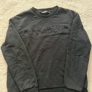Svart sweatshirt från Dolce & Gabbana - Svart sweatshirt från Dolce & Gabbana med broderad logga på bröstet. Tröjan har rund hals, ribbade muddar och är tillverkad i mjuk bomull. Perfekt för dig som gillar stilrena och exklusiva plagg med en clean look.