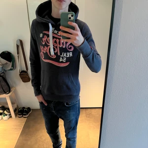 Superdry hoodie  - Tjenare, Säljer en snygg mörkblå hoodie från Superdry, skicket är väldigt bra skulle säga 8/10. Storlek S han på bilden är 180 cm och då sitter den lite litet. Släng iväg dem för frågor! 🙌🍾