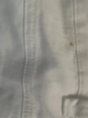 Vita raka jeansbyxor - Snygga vita jeansbyxor med klassisk femficksdesign och raka ben. Byxorna har silverfärgade nitar vid fickorna och bälteshällor. Materialet är bomull och passformen är normal. Perfekt för dig som gillar stilrena och ljusa plagg. Liten fläck bak, syns knappt.