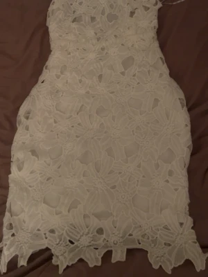 Vit spetsklänning med blommönster - Supersöt vit kort studentklänning med stora blommiga spetsdetaljer. 