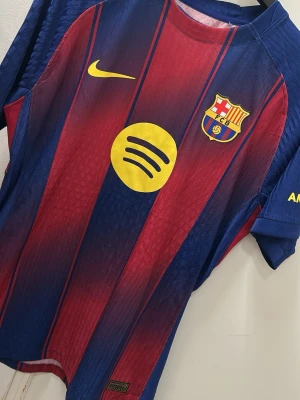 Barça matchtröja Lamine Yamal #10 - Säljer en FC Barcelona matchtröja med Lamine Yamal och nummer 10 på ryggen. Tröjan har klassiska blå och röda ränder, gula detaljer och klubbmärke på bröstet. Tillverkad i lätt polyester med tryckta sponsorer och namn. Perfekt för dig som älskar fotboll och Barça.