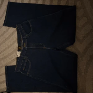 Blå Lee straight jeans hög midja - Säljer ett par klassiska blå jeans från Lee med rak passform och hög midja. Jeansen har fem fickor, gul kontrastsöm och Lee-lapp bak i midjan. Materialet är robust denim och modellen heter 'Jane'. Perfekt för dig som gillar tidlös stil.  Helt Nya med prislapp!