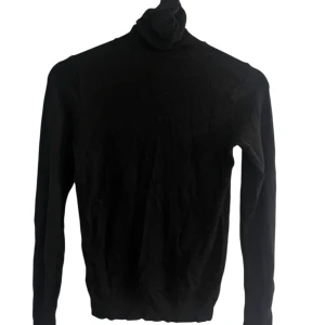 Svart polotröja med lång ärm - En klassisk svart polotröja med lång ärm. Tröjan har en hög krage som kan vikas ner och är tillverkad i ett mjukt material som sitter skönt mot kroppen. Perfekt att styla med jeans eller kjol för en stilren look.