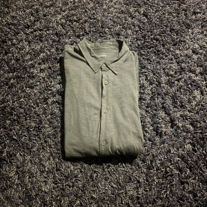 Grå skjorta från Intimissimi - Säljer en stilren grå skjorta från Intimissimi i storlek L. Skjortan har klassisk krage och knäppning framtill med tre knappar. Tillverkad i mjukt och lätt material som känns skönt mot huden. Perfekt för dig som gillar enkel och clean stil.