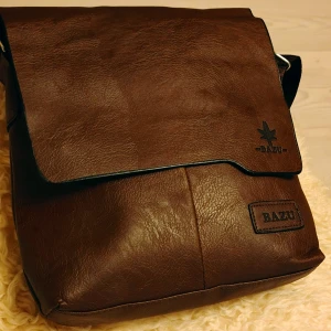 Jeep - BAZU - Axelväska i skinn  - Helt ny messenger-bag/axelväska från tyska Jeep i modell BAZU i äkta skinn med justerbar rem och praktisk dragkedja på baksidan. Väskan har stilren design med lock och diskret logga framtill. Perfekt för att bära dina viktigaste grejer med stil.