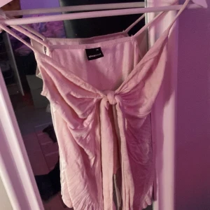 Ljusrosa topp från Gina Tricot - Supersöt ljusrosa topp från Gina Tricot med knyt framtill. Toppen har en flowy och lite asymmetrisk form som ger en chill vibe. Mjukt tyg och tunna band upptill. Perfekt för dig som gillar pastellfärger och snygga detaljer.