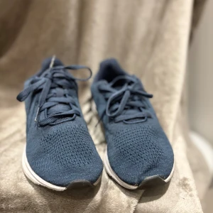Mörkblå sneakers i stickad textil - Säljer ett par mörkblå sneakers från Skechers i storlek 39. Skorna har en stickad ovandel, snörning och vit platt sula. Perfekta för dig som gillar en sportig och clean look. Lätta och bekväma att ha på sig hela dagen.