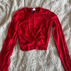 Röd omlottopp  - Säljer en röd långärmad omlottopp från H&M Divided i storlek XS. Toppen är tillverkad i mjuk bomull. Perfekt att styla med jeans eller kjol för en snygg look. Passar även bra till jul eller andra vardagliga tillfällen.