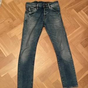 Slim fit jeans från Jack & Jones - Snygga blå slim fit jeans från Jack & Jones med klassisk femficksdesign, slitna detaljer och ljus tvätt. Byxorna har normal midja, knappgylf och coola sömmar på bakfickorna. Perfekt för dig som gillar en smal och modern siluett. W28 L30