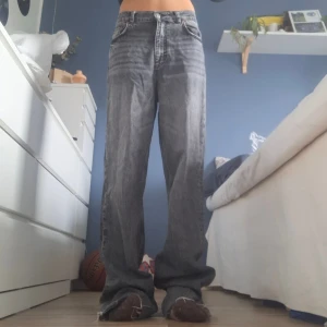 Gråa raka jeans med råa kanter - Säljer ett par gråa/svarta zara jeans med rak passform och hög midja. Jeansen har klassisk femficksdesign, dragkedja och knapp framtill samt råa, fransiga benslut. Aldrig använda då de var lite för stora för mig.