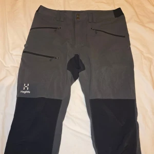Haglöfs friluftsbyxor - Säljer nu ett par friluftsbyxor från Haglöfs i grått och svart med flera dragkedjeförsedda fickor. Perfekta för utomhusaktiviteter och äventyr, med bekväm passform och slitstarkt material🚀
