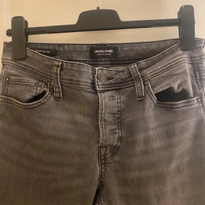 Grå slim jeans från Jack & Jones - Snygga grå jeans från Jack & Jones i modellen Slim/Glenn. Jeansen har fem fickor, klassisk knappstängning och smal passform som sitter riktigt bra. Materialet är mjukt och stretchigt jeans, perfekt för dig som gillar en modern look.