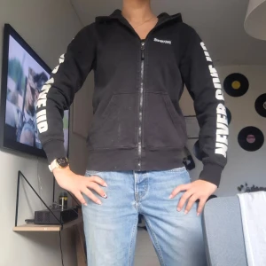 Svart hoodie med peppande tryck - Svart hoodie från Imperious Sport med stora vita tryck på ärmarna: 'NEVER GIVE UP' och peppande citat på ryggen i vitt och rosa. Huva med logga och dragkedja framtill.