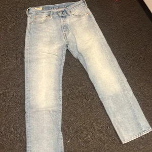 Levi's 501 ljusblå jeans straight fit - Ljusblå Levi's 501 jeans med klassisk femficksdesign och raka ben. Jeansen har en snygg tvättad look och ikonisk läderpatch bak i midjan. Perfekta för dig som gillar en avslappnad och tidlös stil.