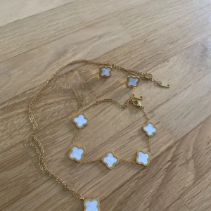 Guldigt halsband och armband med vita klöver och örhängen  - Säljer ett matchande set med halsband och armband i guldfärgad metall. Båda har flera vita klöverformade hängen med guldkant, vilket ger en lyxig och trendig vibe. Perfekt för dig som gillar unika detaljer och vill sticka ut med snygga accessoarer.