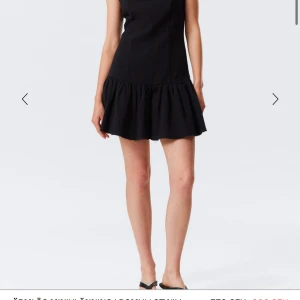 Svart kort klänning med volang - Supersnygg svart kort klänning med volang nedtill och öppen rygg. Klänningen är ärmlös och har en stilren, figurnära passform med lätt struktur i tyget. Perfekt för dig som gillar minimalistisk stil med en twist.