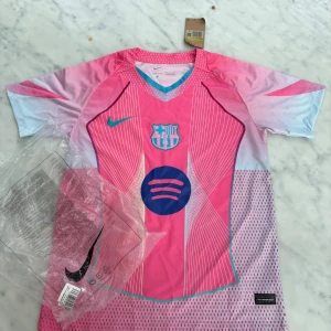 FC Barcelona rosa matchtröja Nike S - FC Barcelona fotbollströja från Nike i en riktigt snygg rosa färg med vita och blå detaljer. Tröjan har klubbmärke och sponsortryck på bröstet, korta ärmar och är tillverkad i lätt Dri-Fit material som andas. Perfekt för dig som vill sticka ut på planen.