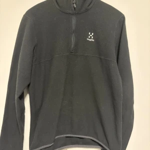 Svart fleece-tröja från Haglöfs - Svart fleece-tröja från Haglöfs i storlek L för dam. Tröjan har half zip framtill, långärmad design och diskret logga på bröstet. Perfekt för kyliga dagar och outdoor-aktiviteter. Mjuk och skön känsla med klassisk passform. (Använt några få gånger) köptes för 1300kr drf är de lägsta 500kr