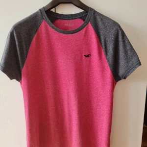 Röd och svart t-shirt från Hollister strl S - Snygg t-shirt från Hollister i en fräsch röd färg med kontrasterande svarta ärmar. Den har en liten logga på bröstet och korta ärmar. Storlek S. Kan hämtas i Vallentuna.