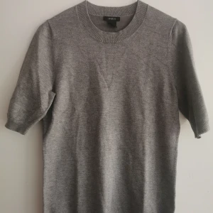 Grå finstickad kortärmad tröja från Lindex - En stilren grå stickad tröja från Lindex med rund halsringning och kortare ärmar. Tröjan har en klassisk passform och är perfekt ensam eller under kavaj. . Mjuk och skön känsla tack vare det stickade materialet.