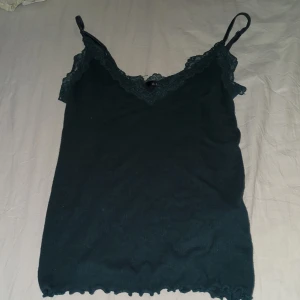 Mörkgrön linnetopp med spets - Supersnygg mörkgrön linnetopp från Amisu med justerbara axelband och v-ringning dekorerad med spets. Toppen är ribbad och har volangkant nertill för en extra detalj. Perfekt att styla med jeans eller kjol för en trendig look.