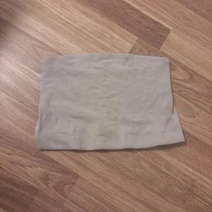 Beige bandeau tubtopp - Säljer en enkel och stilren beige bandeau tubtopp. Toppen är ärmlös och har en rak, tight passform som sitter snyggt över bröstet. Perfekt att matcha med höga jeans eller kjol för en clean look.
