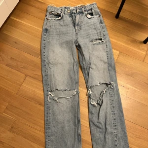 Ljusblå ripped jeans från Perfect Jeans - Ljusblå jeans från Perfect Jeans med rejält slitna detaljer och stora hål vid knäna samt fransig midja. Klassisk femficksmodell i rak passform, tillverkad i bomull. Perfekta för dig som gillar en edgy och avslappnad stil. Har mycket hål där bak därför billigt pris