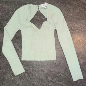 Mintgrön ribbad topp & Other Stories - Superfin mintgrön ribbad topp från & Other Stories med lång ärm och unik öppen rygg med knäppning. Toppen har en snygg v-ringad form framtill och är croppad. Perfekt för dig som vill sticka ut med en cool detalj på ryggen.