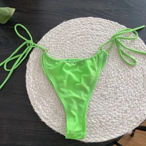 Limegrön bikiniunderdel med knyt - Snygg limegrön bikiniunderdel med höga ben och smala sidor som knyts med långa band. Modellen är enkel och stilren, perfekt för strandhäng. Materialet är mjukt och stretchigt syntet som sitter skönt mot huden.